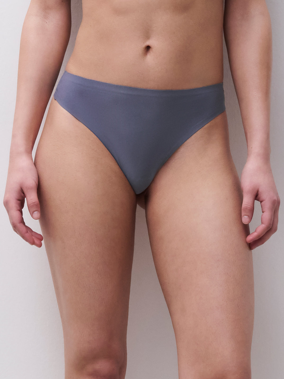 A model wearing a solid slate blue bikini bottom, shown from the waist to the upper thighs against a neutral light gray background.
