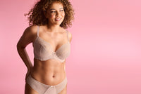 Woman wearing a beige bra and panties set against a pink background