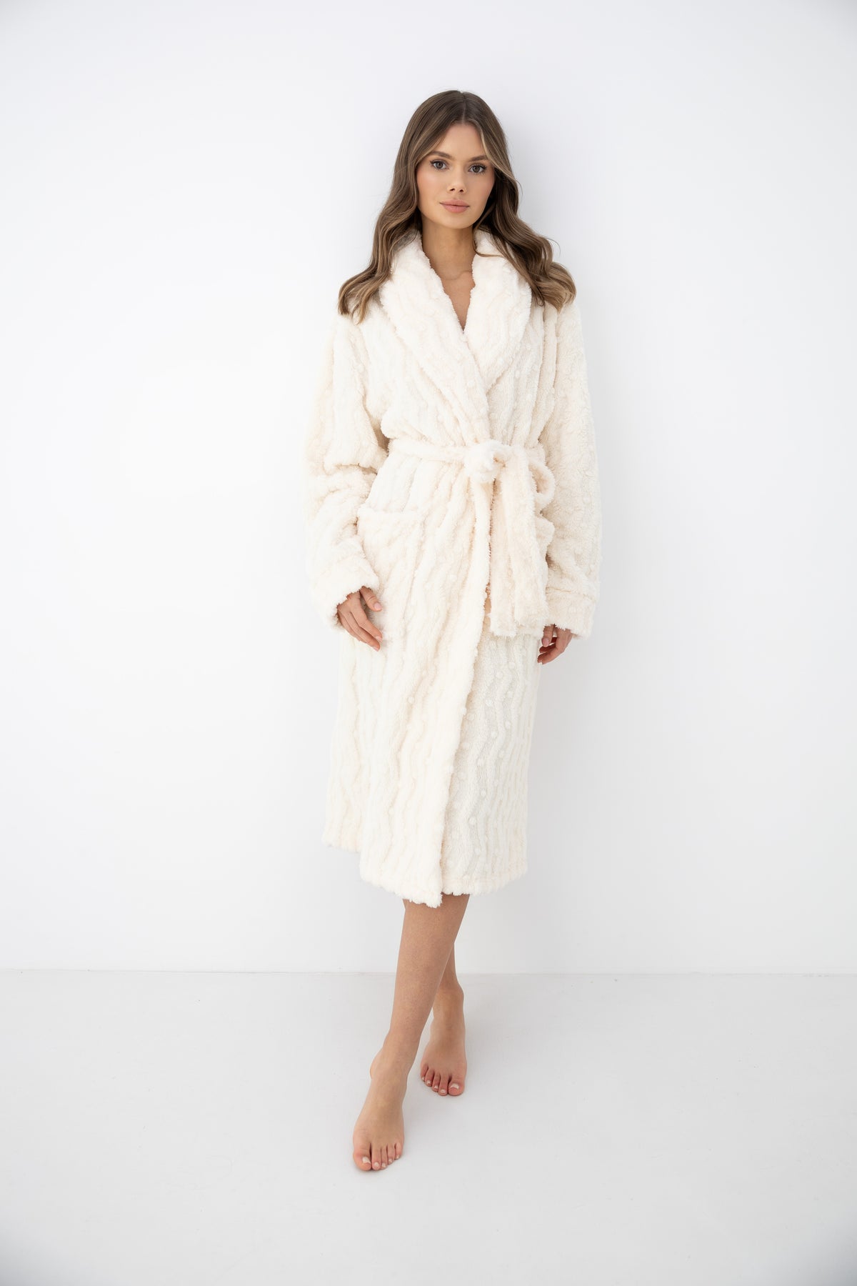 A woman modeling a plush, textured cream-colored bathrobe against a clean white studio background.