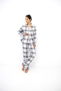 A woman modeling a matching plaid pajama set consisting of a long-sleeve button-up shirt and wide-leg pants, standing against a plain white studio background.