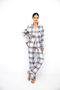 A woman modeling a matching plaid pajama set consisting of a long-sleeve button-up shirt and wide-leg pants, featuring a gray, white, and black checkered pattern, against a plain white studio background.