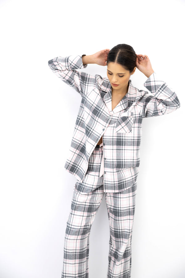 A woman wearing a gray, white, and black plaid pajama set, standing against a plain white background with her hands in her hair.