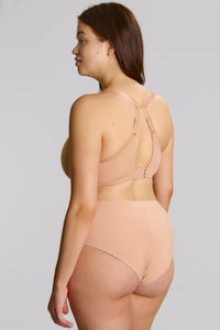 A woman shown from the back wearing a nude-beige seamless bra and matching high-waisted briefs against a solid light gray studio background.