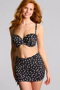 Woman wearing a black polka dot bikini with a matching skirt on a gray background