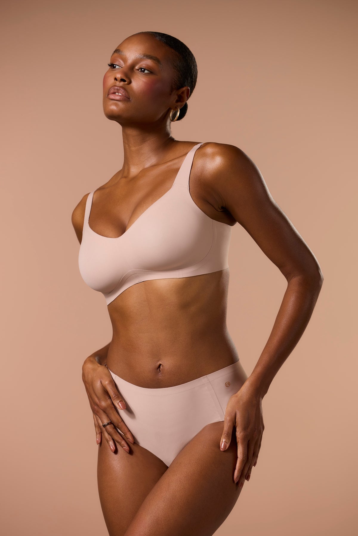Woman wearing a beige bra and panties set against a beige background