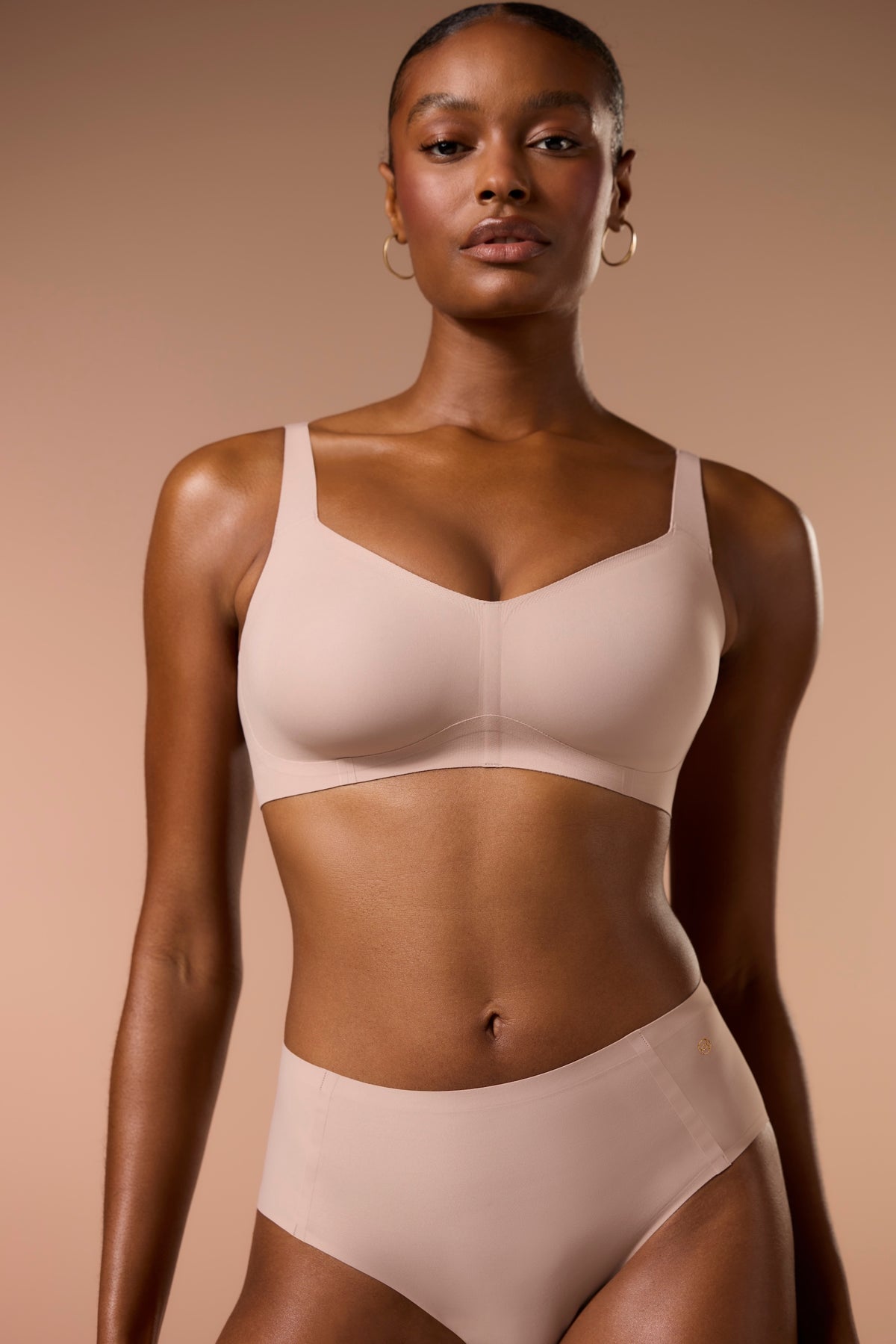 Woman wearing a beige bra and panties set against a beige background