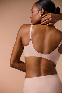 Woman wearing a beige bra and underwear set with a neutral background