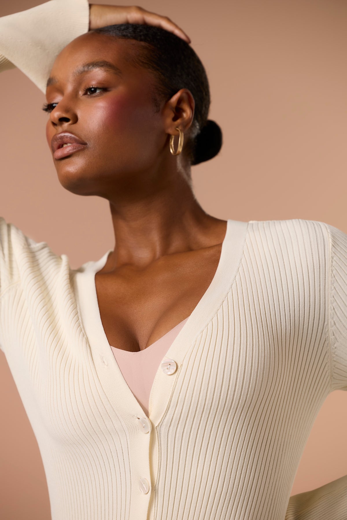 Woman wearing a cream-colored ribbed cardigan against a beige background