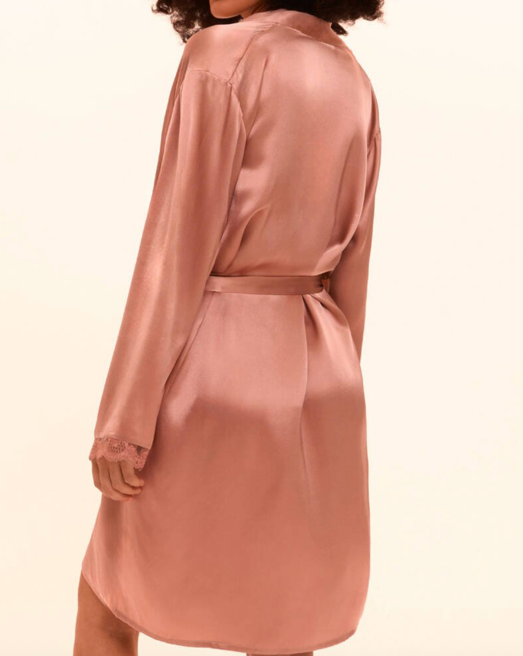 Person wearing a pink silk robe on a beige background