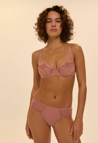 Woman wearing a pink bra and panties set against a beige background