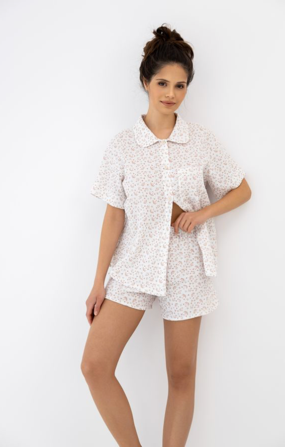 Woman wearing a white patterned shirt and shorts set on a plain background