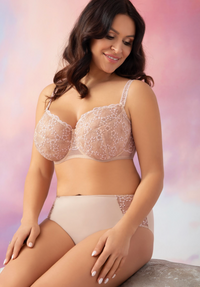 Woman wearing a beige lace bra and panties set against a soft pink background