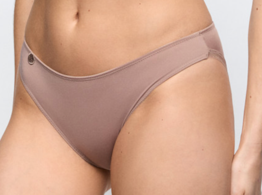 A close-up of a model wearing a low-rise, high-cut bikini bottom in a muted taupe-brown color. The underwear features a small metallic button on the left side of the waistband.
