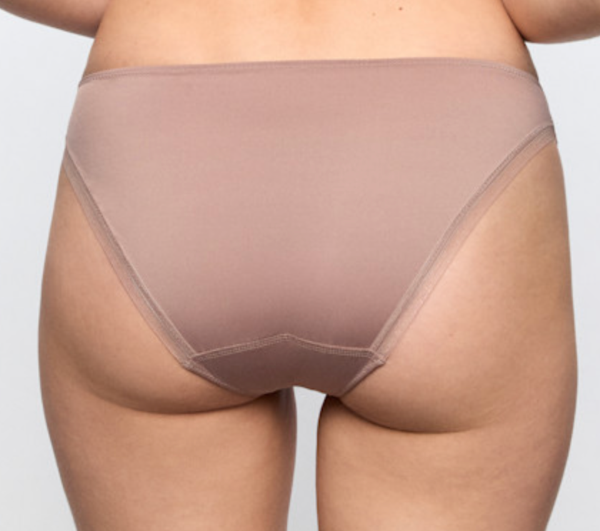 Rear view of a person wearing a sheer, nude-toned high-waisted brief or shapewear bottom against a light gray studio background.