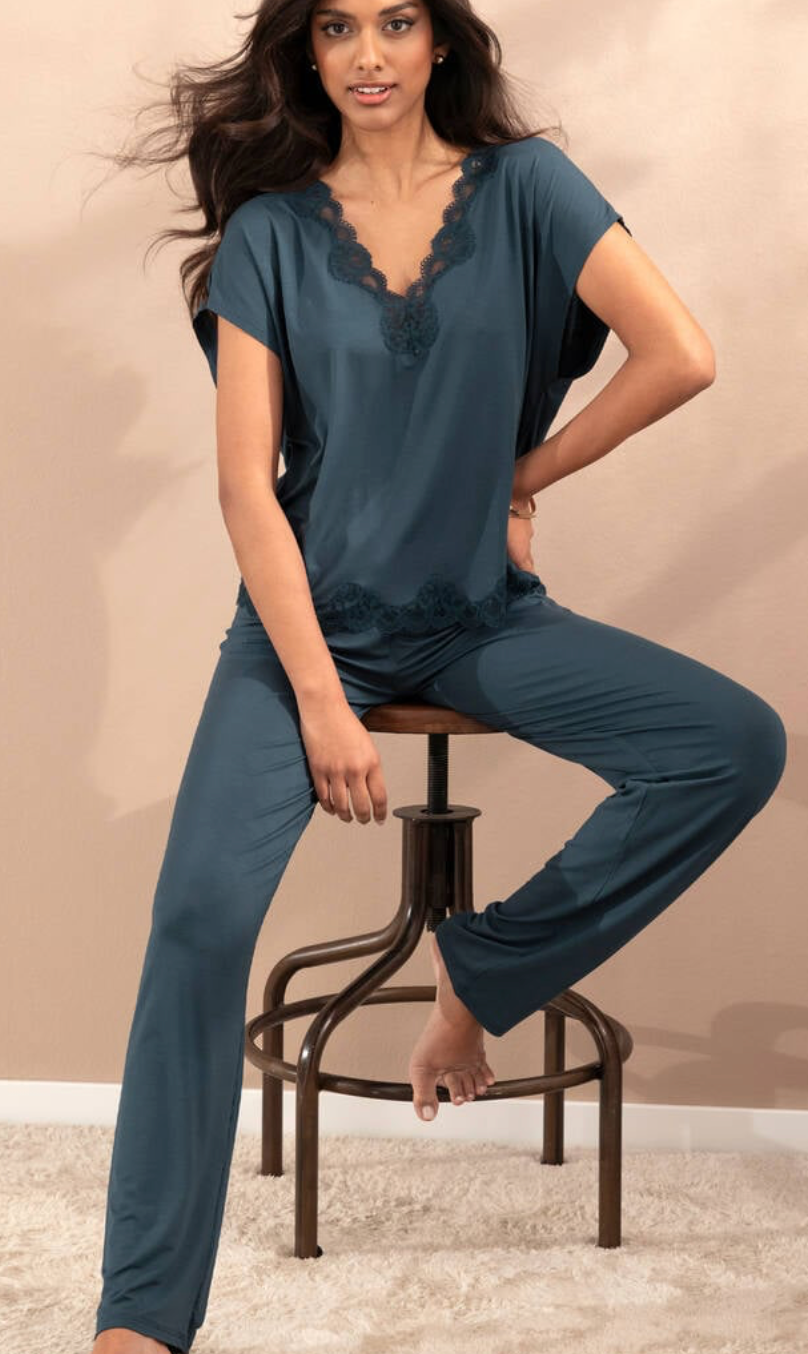A woman models a two-piece sleepwear set consisting of a short-sleeve top and matching pants in a muted teal-blue color. The set features lace trim details along the scoop neck and waist.