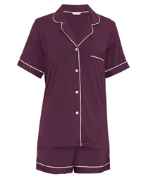 A two-piece short-sleeve pajama set in deep plum purple, featuring white piping trim along the collar, cuffs, pocket, and hem, with white buttons on the shirt front.