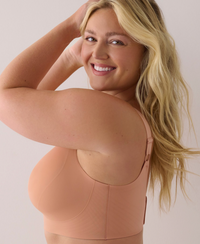 A smiling blonde woman wearing a peach-colored wireless bra, looking back over her shoulder against a plain light background.