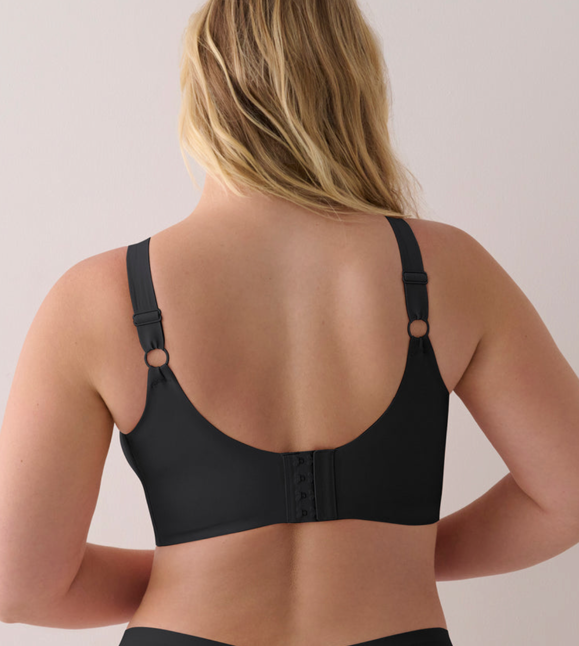A woman shown from the back wearing a black bra with adjustable straps and a lace-up back closure, photographed against a plain light background.