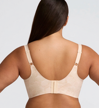 Rear view of a woman wearing a beige bra with adjustable straps and a subtle tonal pattern, shown against a light gray studio background.