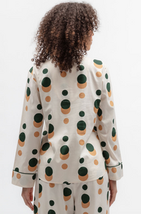 A model viewed from behind wearing a matching pajama set with a pink cream base and a bold green and tan polka dot pattern.
