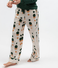 A person wearing loose light pink lounge pants with a large green and tan polka dot pattern, paired with a dark green long-sleeve top, shown against a plain white studio background.