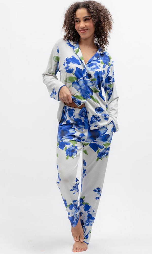 A woman modeling a two-piece satin pajama set with a blue floral print on a white background, standing against a plain white studio backdrop.