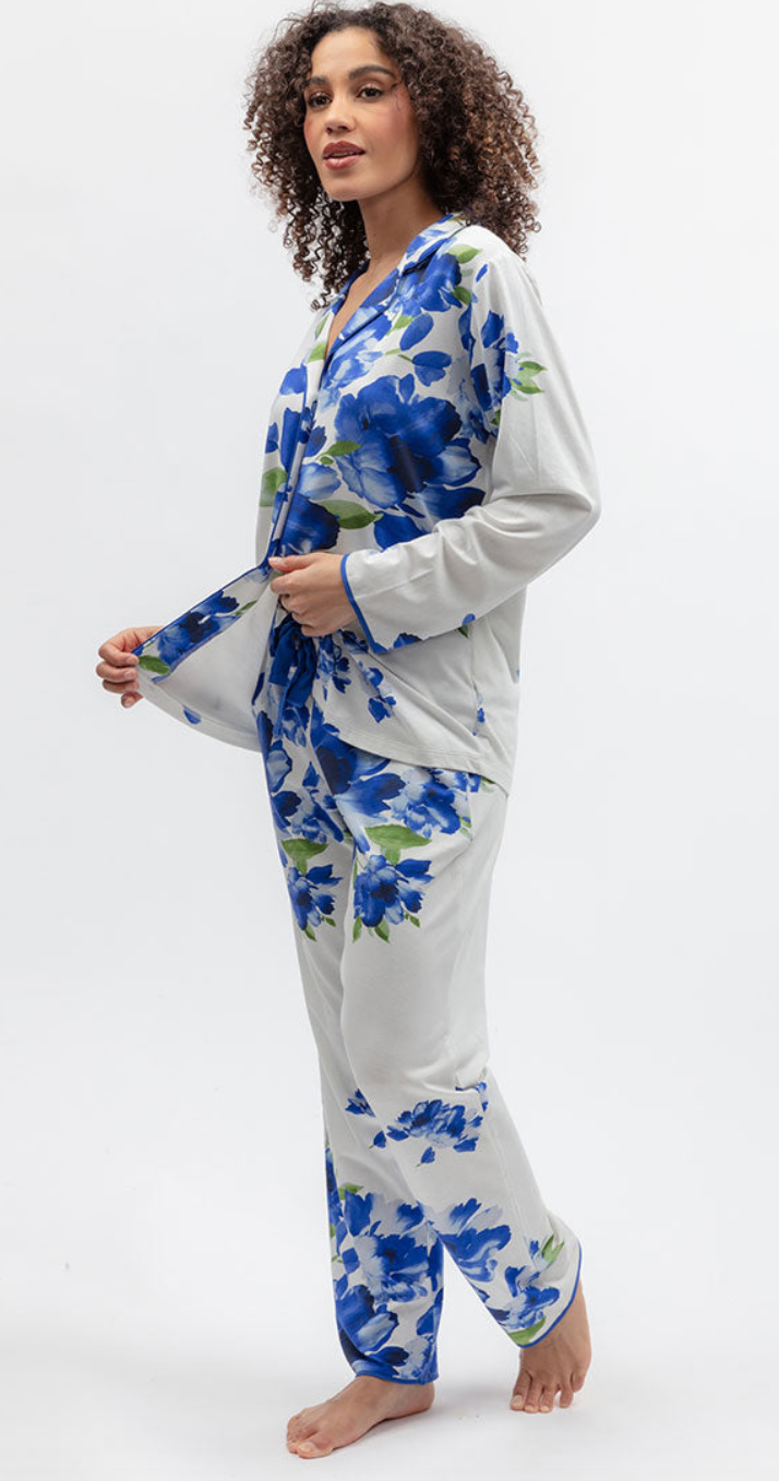A woman modeling a two-piece pajama set with a white base and a blue floral print, standing against a plain white studio background.