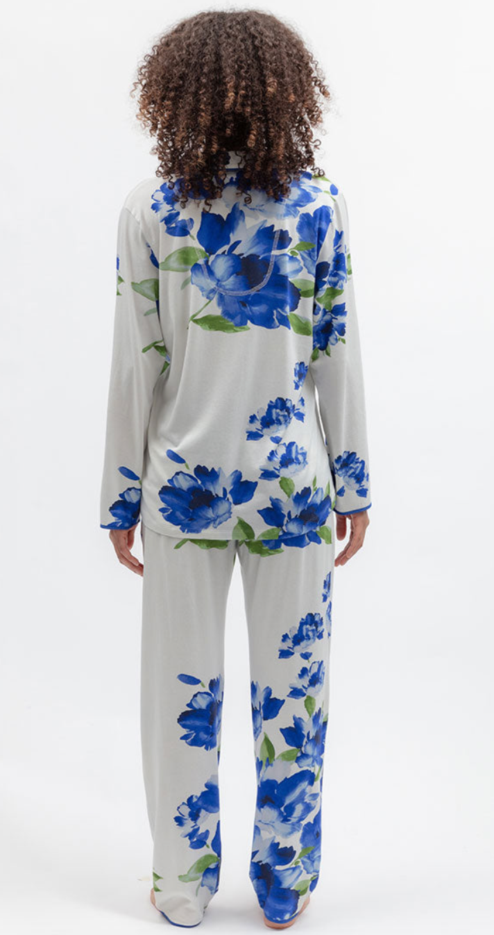 A woman viewed from behind wearing a matching long-sleeve pajama set with a blue floral print on a white base, photographed against a clean white studio background.
