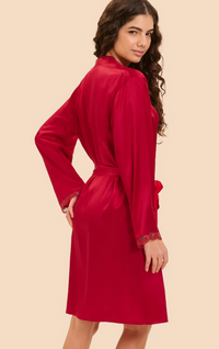 A woman modeling a red silk robe with lace cuffs, shown from a three-quarter back angle against a solid beige background.