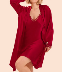 A woman modeling a matching red silk slip dress and long open-front robe with lace trim, posed against a plain light beige studio background.
