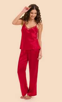 A woman modeling a two-piece red silk pajama set consisting of a camisole top with lace trim and matching wide-leg pants, set against a solid beige background.