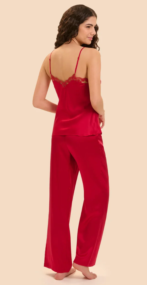 A woman modeling a bright red two-piece silk pajama set, featuring a camisole top with lace trim on the back and matching wide-leg pants, shown from a rear three-quarter view against a solid beige background.