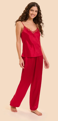 A woman modeling a two-piece red silk pajama set with a camisole top featuring lace trim and matching wide-leg pants, set against a solid light beige background.