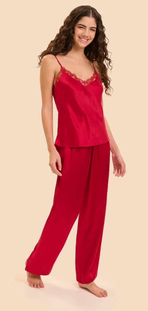 A woman modeling a two-piece red silk pajama set with a camisole top featuring lace trim and matching wide-leg pants, set against a solid light beige background.