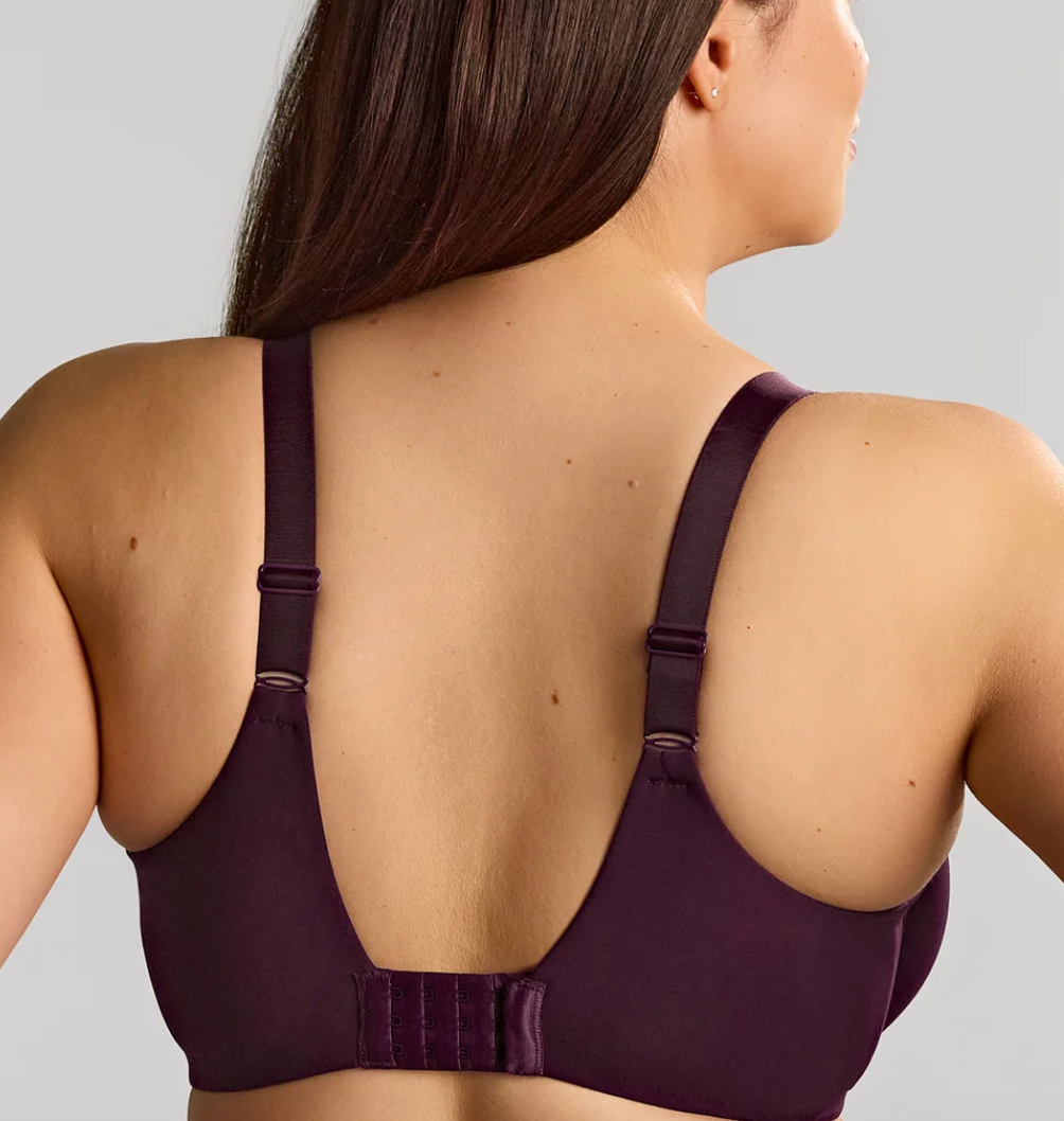 Rear view of a woman wearing a dark plum purple wireless bra with adjustable straps and a wide underband, shown against a solid light gray background.