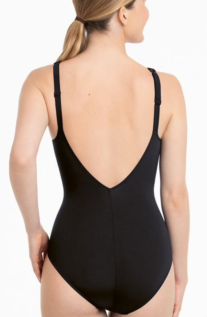 A woman shown from the back wearing a black one-piece swimsuit with a deep V-shaped open back and thin shoulder straps, against a plain white studio background.