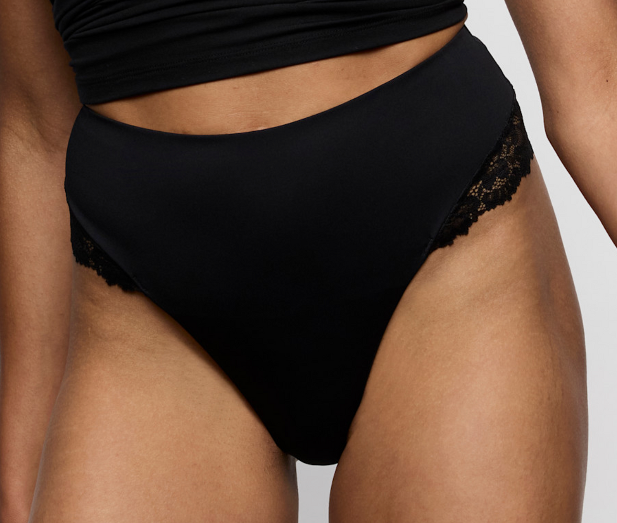 Black high-waisted briefs with black lace trim on the sides, shown on a model against a light gray background.