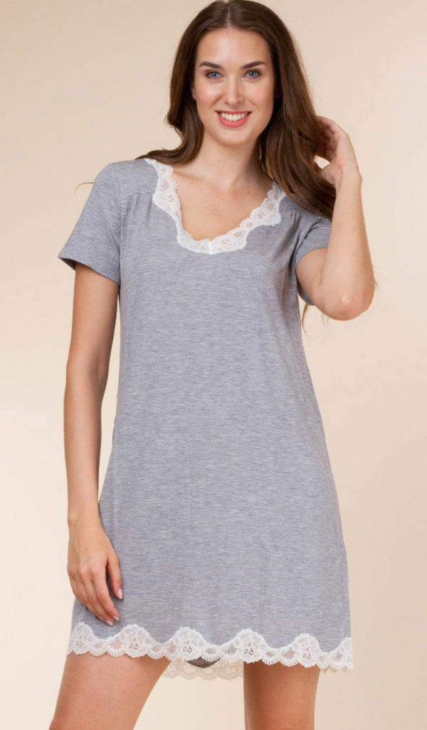 A woman wearing a short-sleeve gray nightgown with white lace trim at the neckline and hem, photographed against a plain beige studio background.