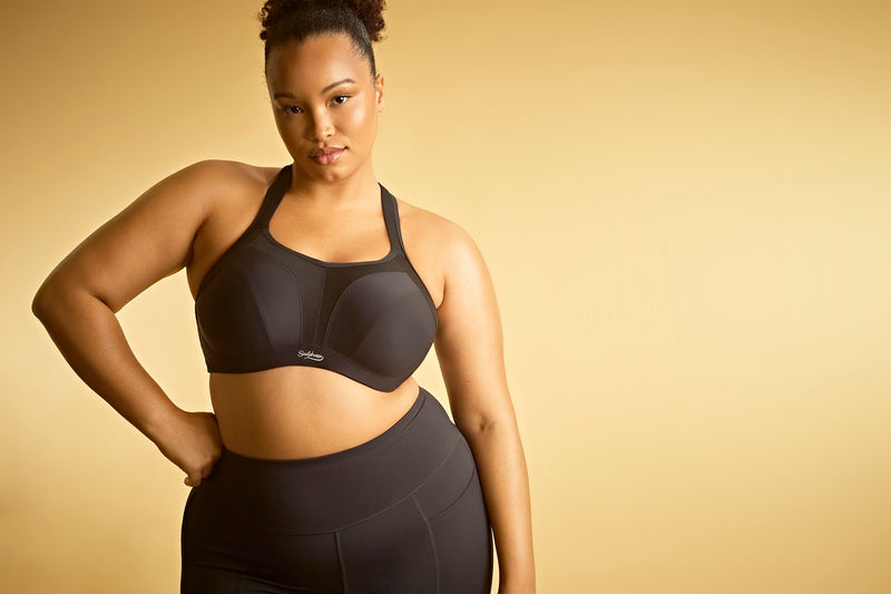 Woman wearing a black sports bra and leggings on a gold background