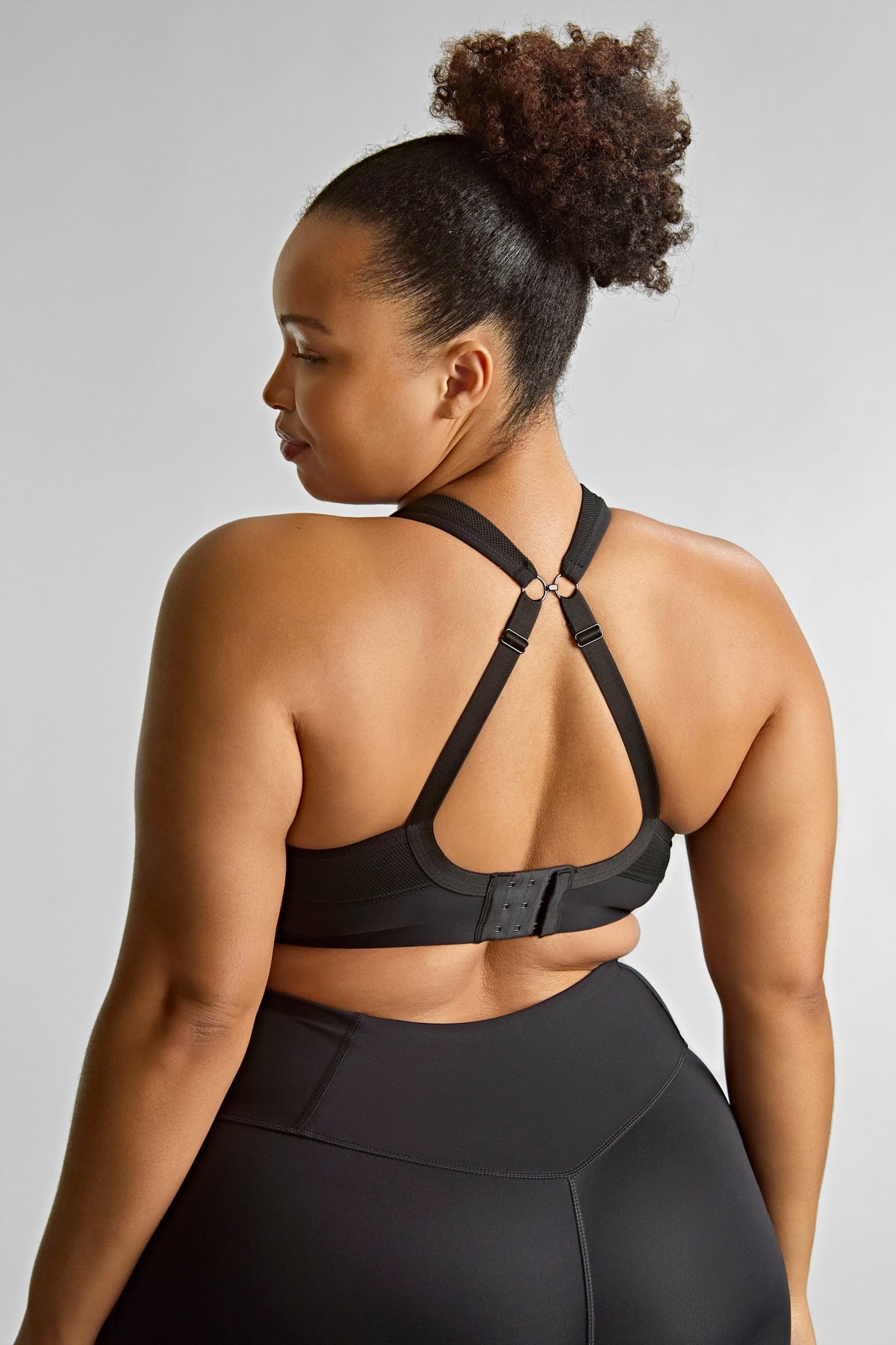 Woman wearing a black sports bra and leggings on a light gray background
