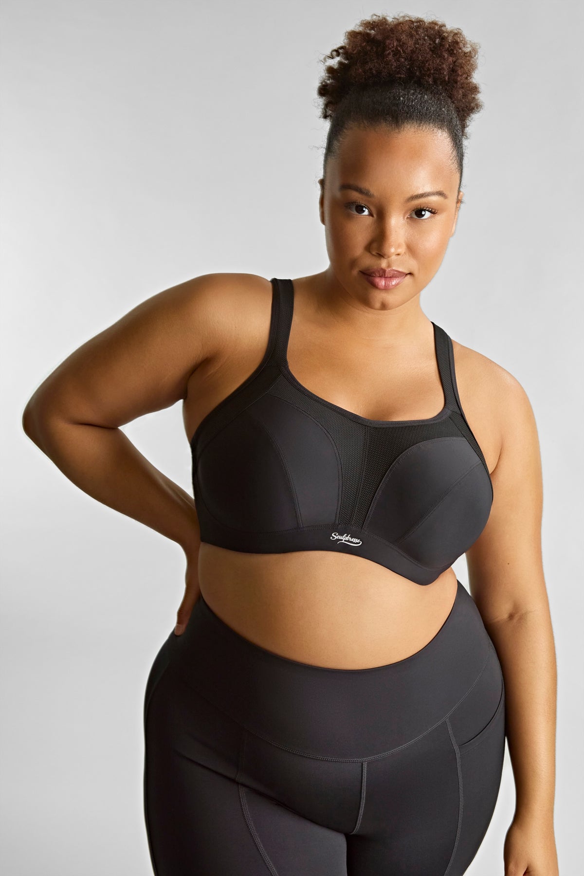 Woman wearing a black sports bra and leggings on a light gray background