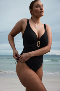 Woman wearing a black swimsuit with a gold buckle on a beach