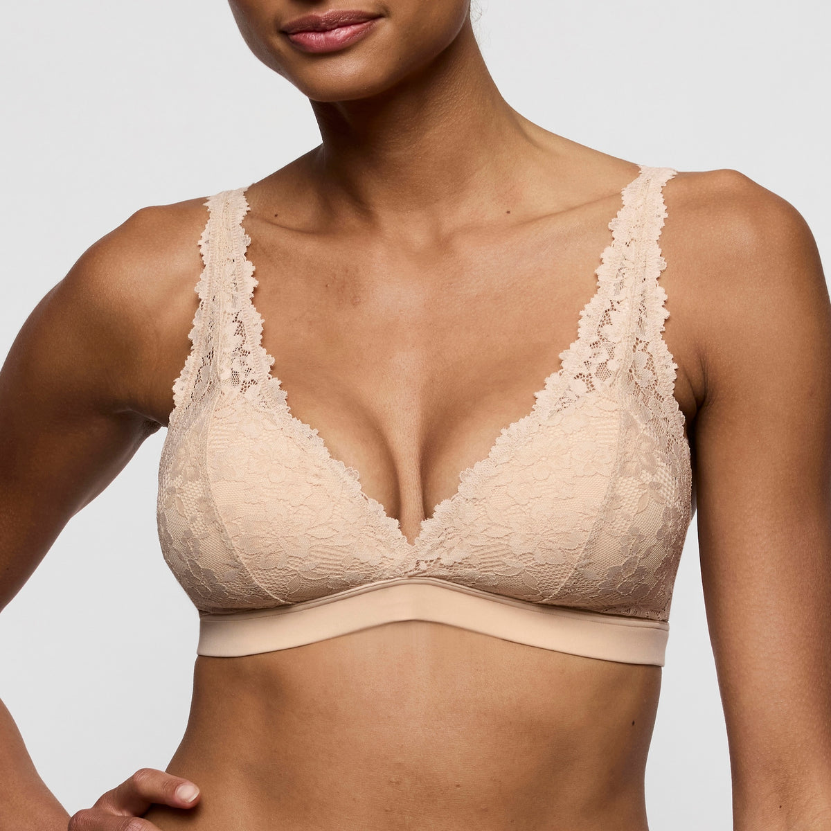 Beige lace bra worn by a model on a plain background