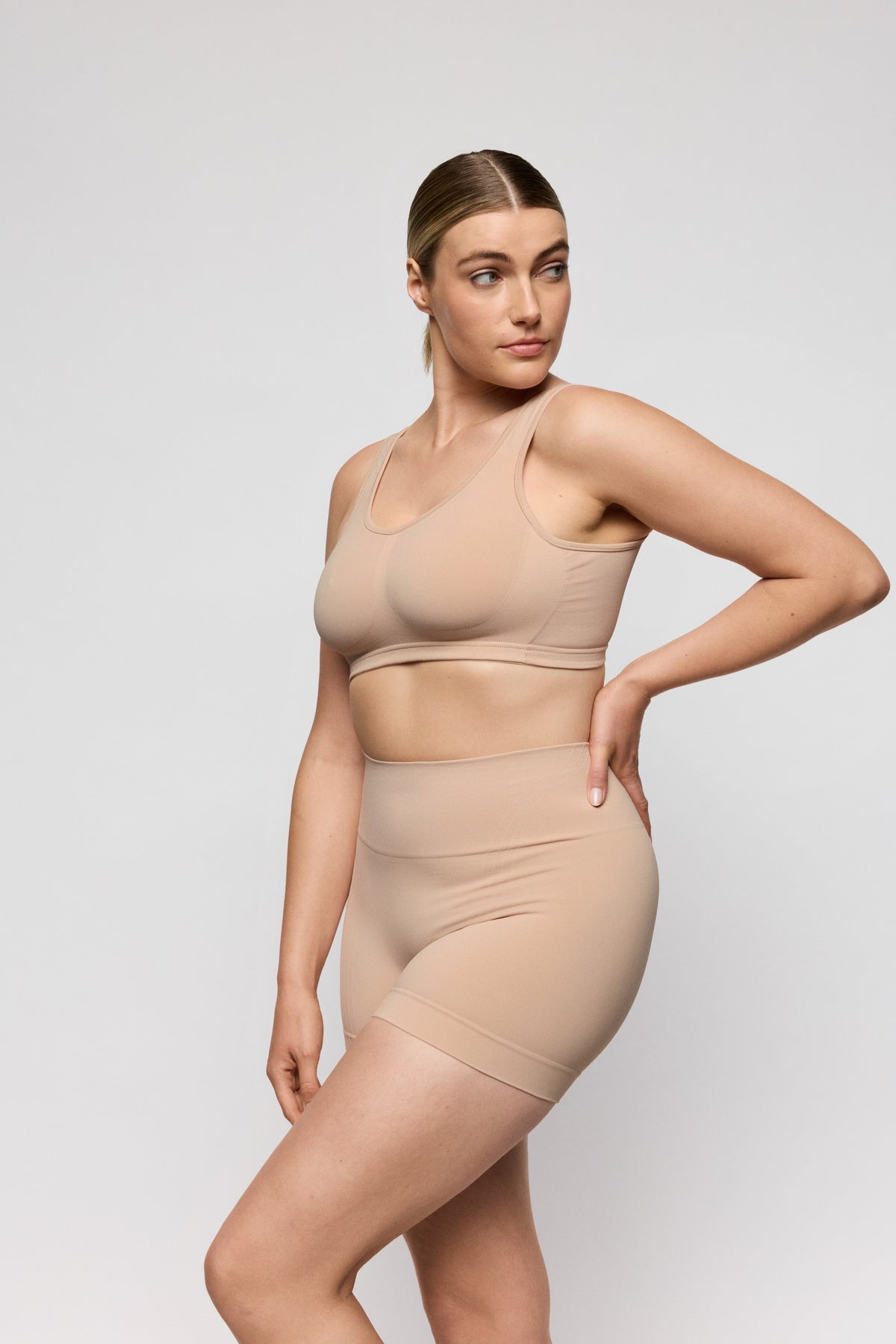 Woman wearing a beige shapewear outfit on a light gray background