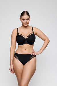 A woman modeling a black two-piece lingerie set consisting of a strappy underwire bra and matching high-waisted briefs with sheer mesh side panels, set against a plain light gray studio background.