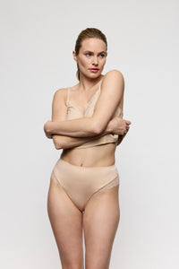 Woman wearing beige lingerie against a plain background