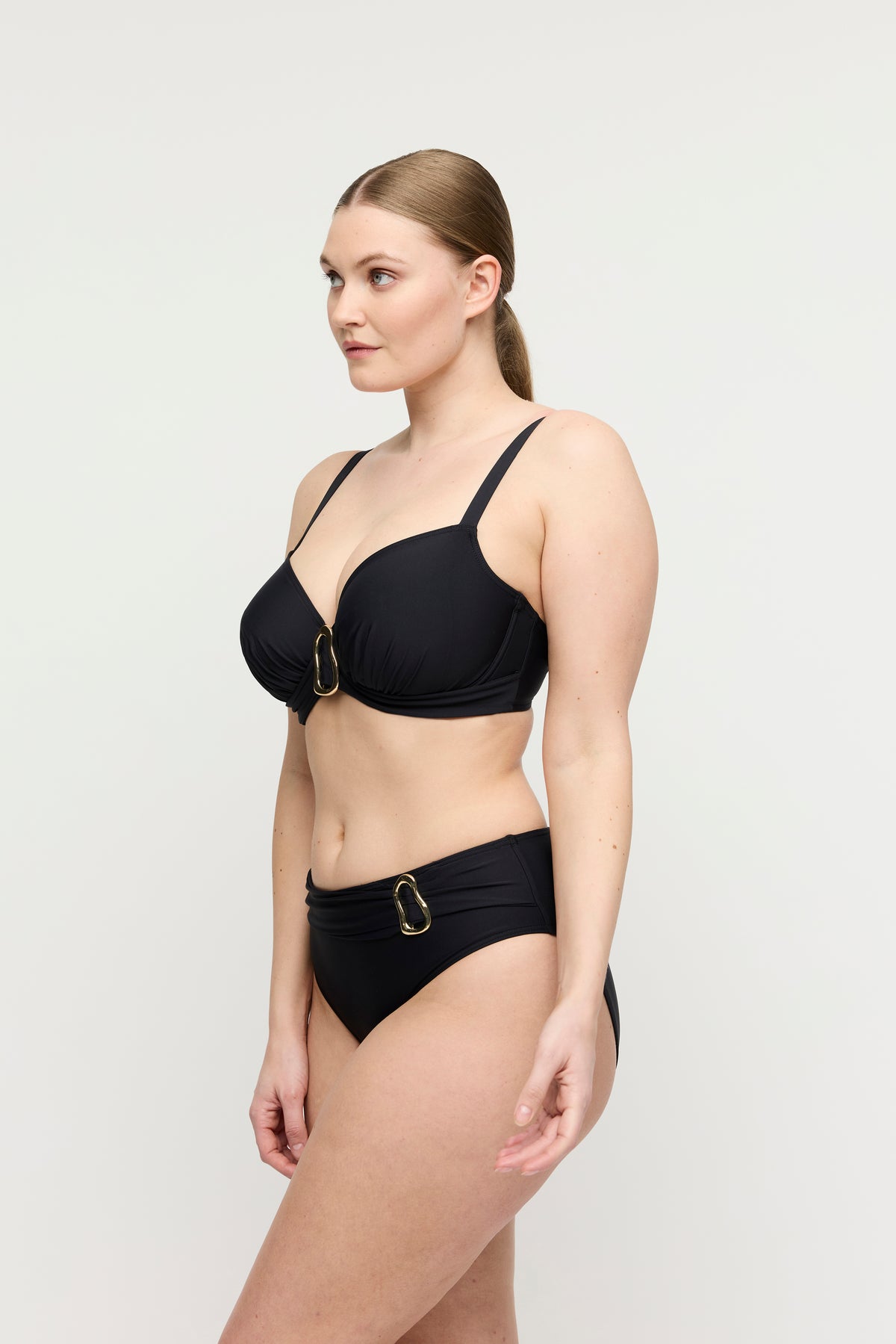 Woman wearing a black bikini with gold hardware on a white background