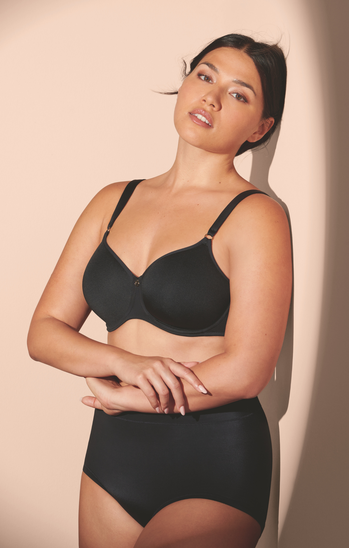 Woman wearing a black bra and underwear set against a beige background