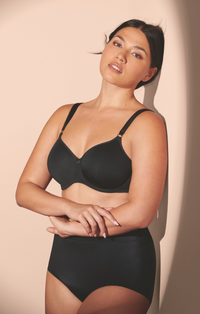 Woman wearing a black bra and underwear set against a beige background
